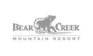Gray logo of Bear Creek Mountain Resort featuring a bear walking between the words "Bear" and "Creek," with "Mountain Resort" written below.