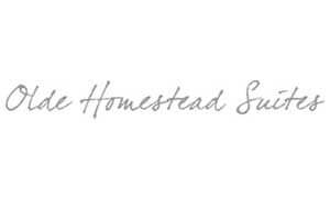 The image shows the text "Olde Homestead Suites" written in a gray, cursive font on a white background.