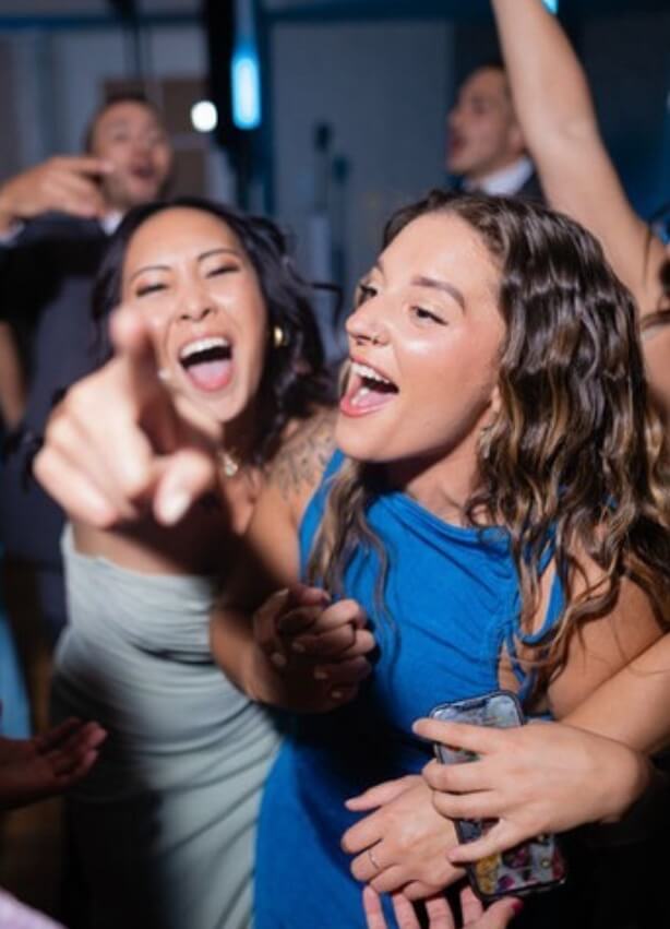 Lehigh Valley Private Event DJs Two women smiling and laughing at a lively indoor event, with one pointing toward the camera and others celebrating in the background.