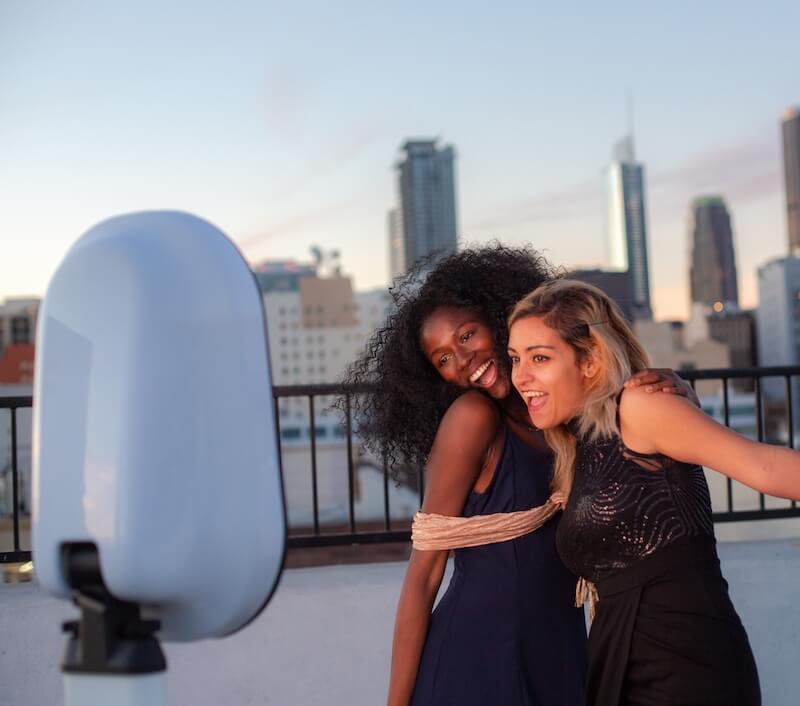 corporate photo booth rental Two women smiling and posing together for a photo on a rooftop with a city skyline in the background.